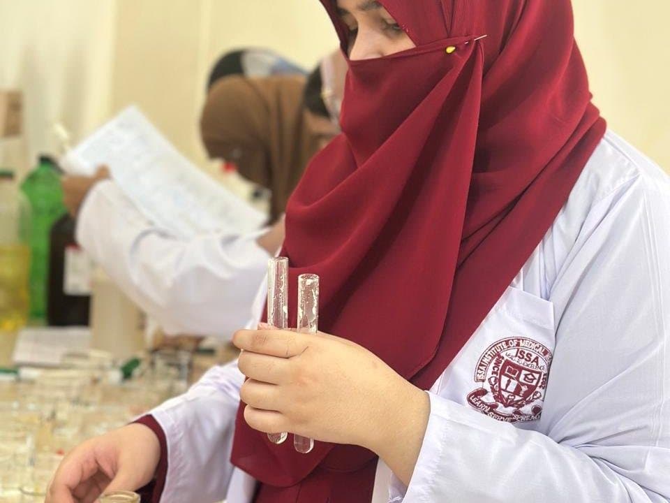 An ISSA student in a white coat holding test tubes in the laboratory