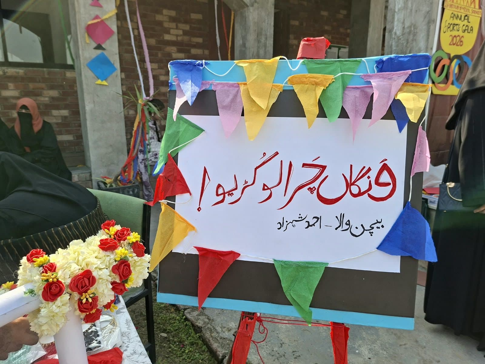 A Culture Day sign in Urdu decorated with bunting and flowers on the ISSA campus