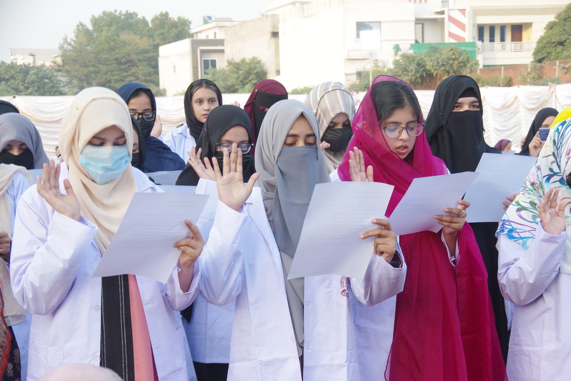 Students in white coats raising their right hands as they read the oath at Orientation Day