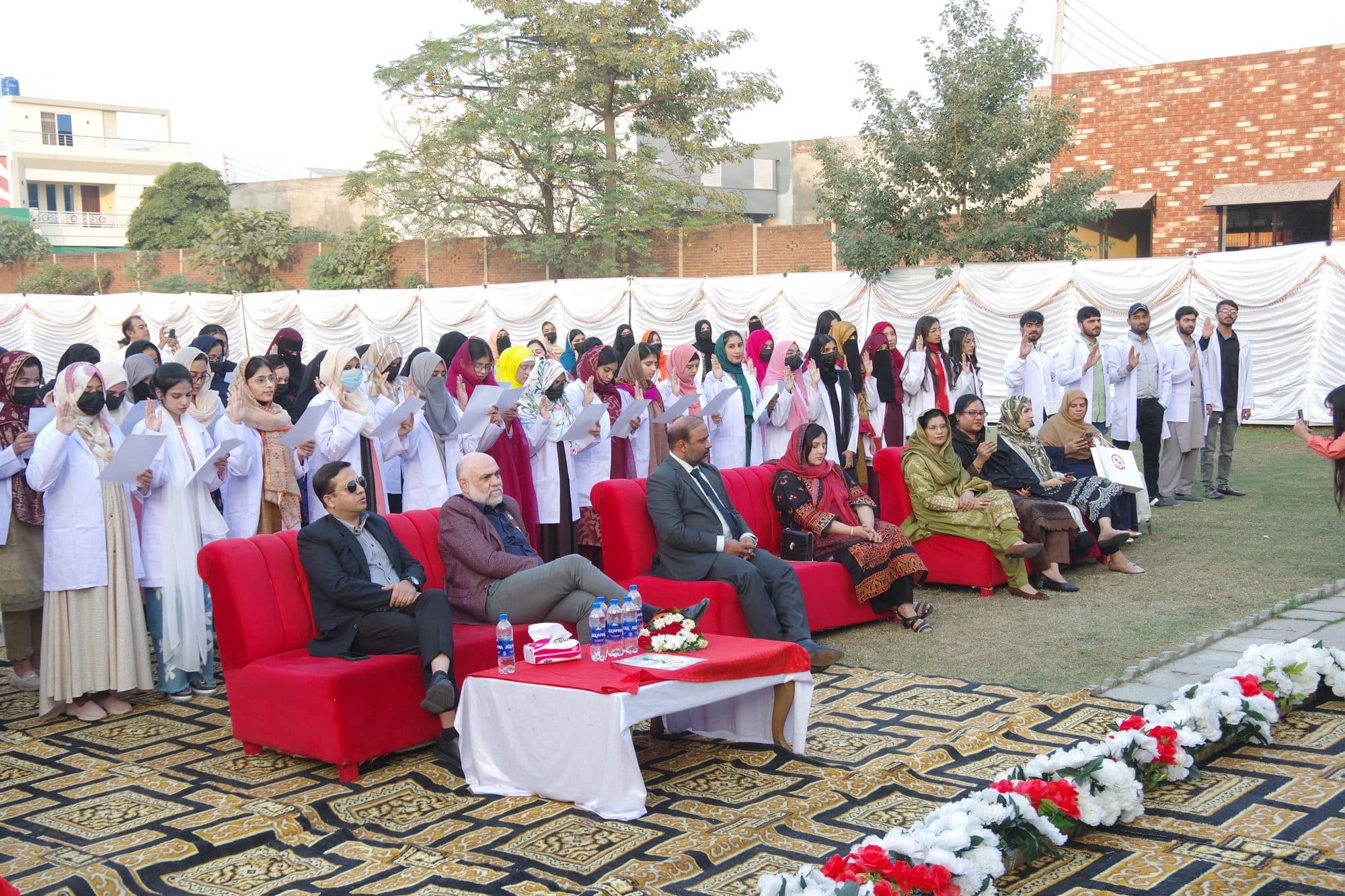 Rows of new students in white coats taking the oath behind seated guests