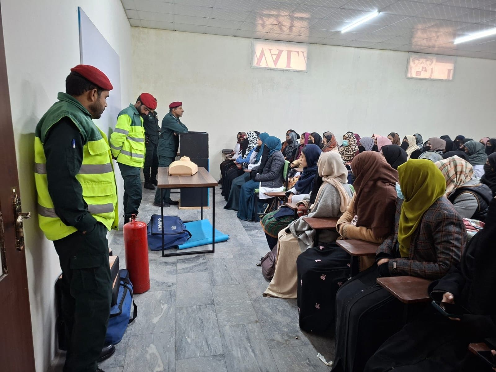 Rescue 1122 trainers with a CPR manikin, first-aid kit and fire extinguisher in front of students