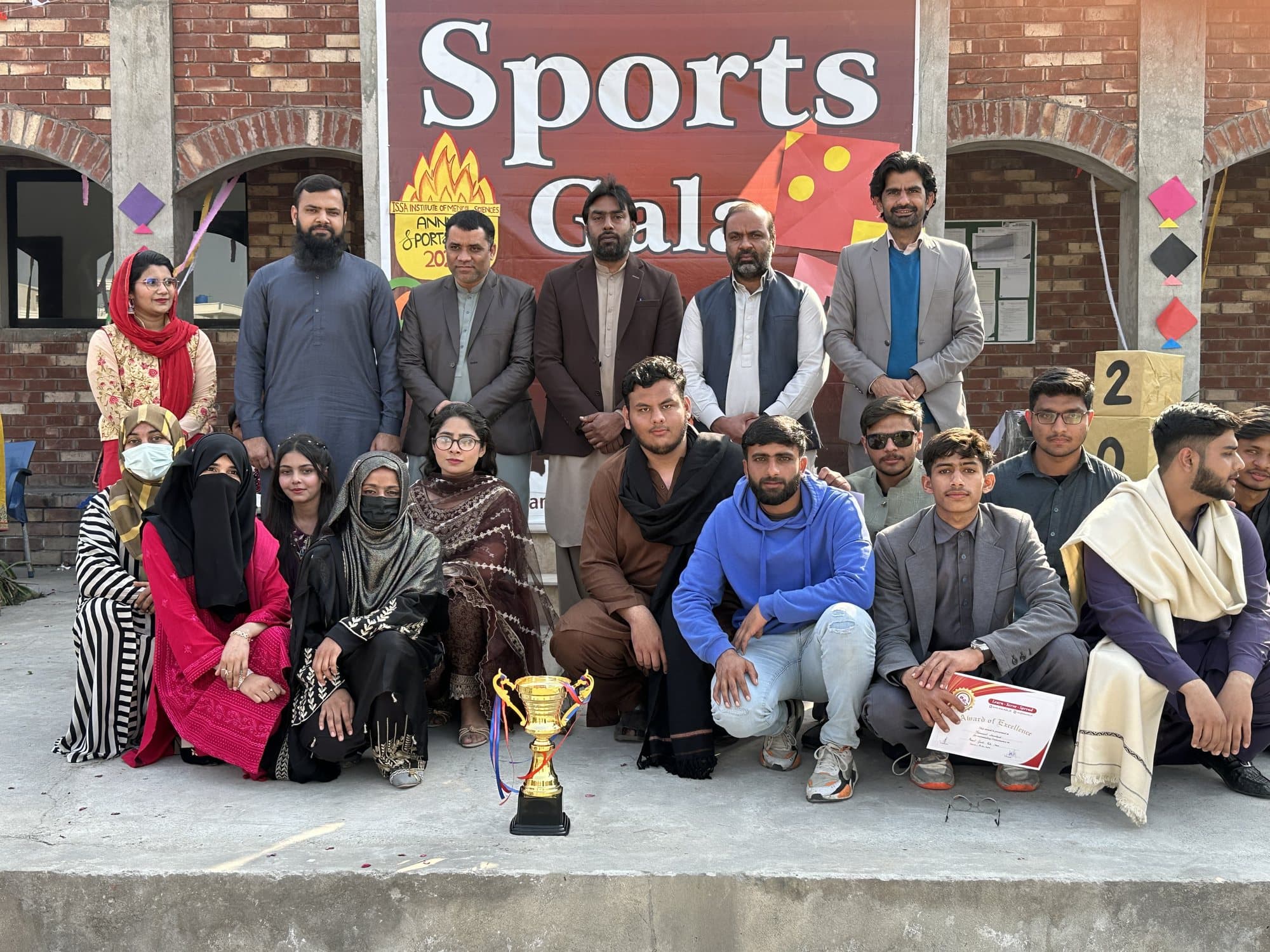 Faculty and students with a trophy and certificate in front of the Sports Gala banner