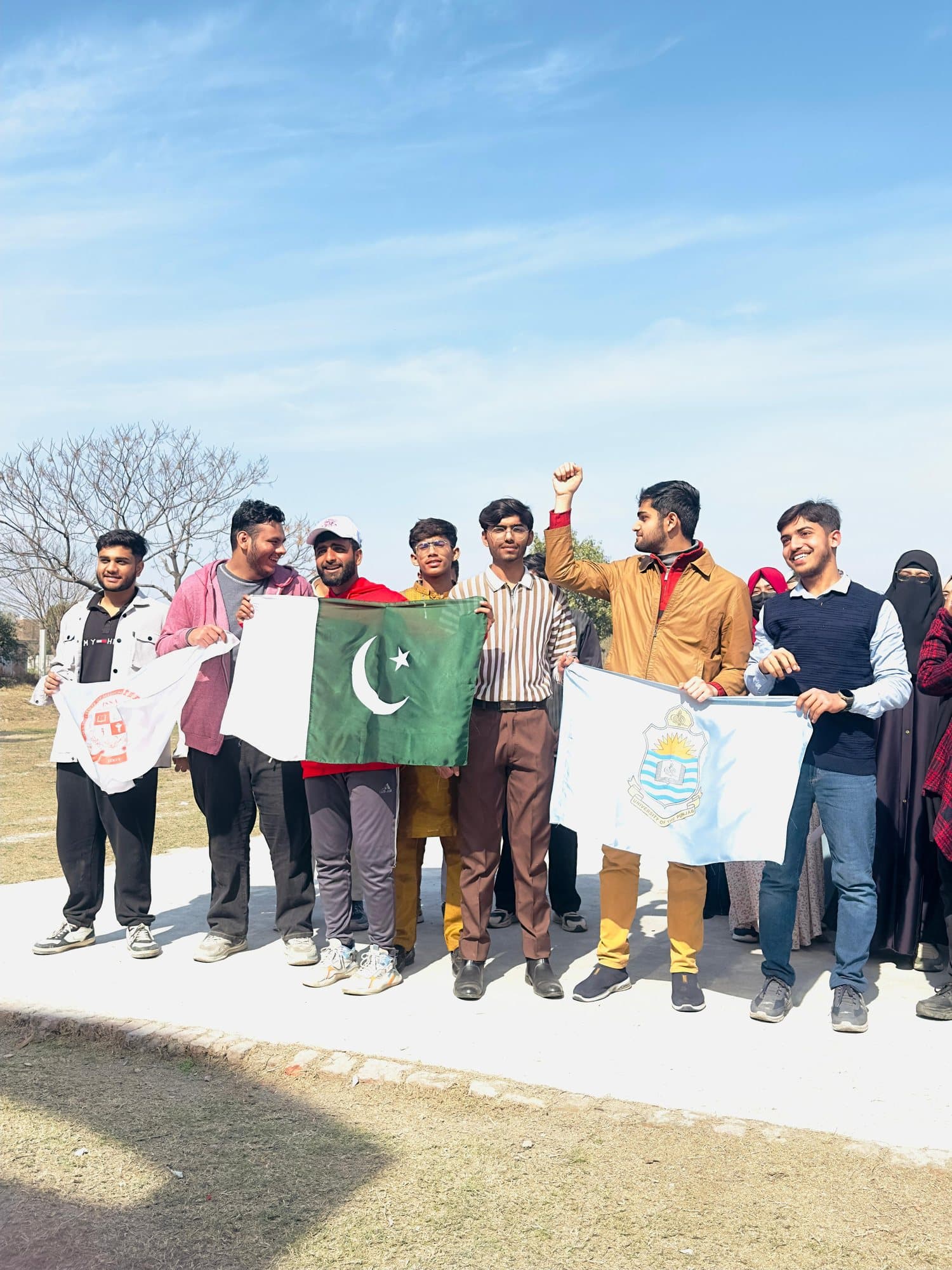 Students holding the ISSA, Pakistan and University of the Punjab flags on the sports ground