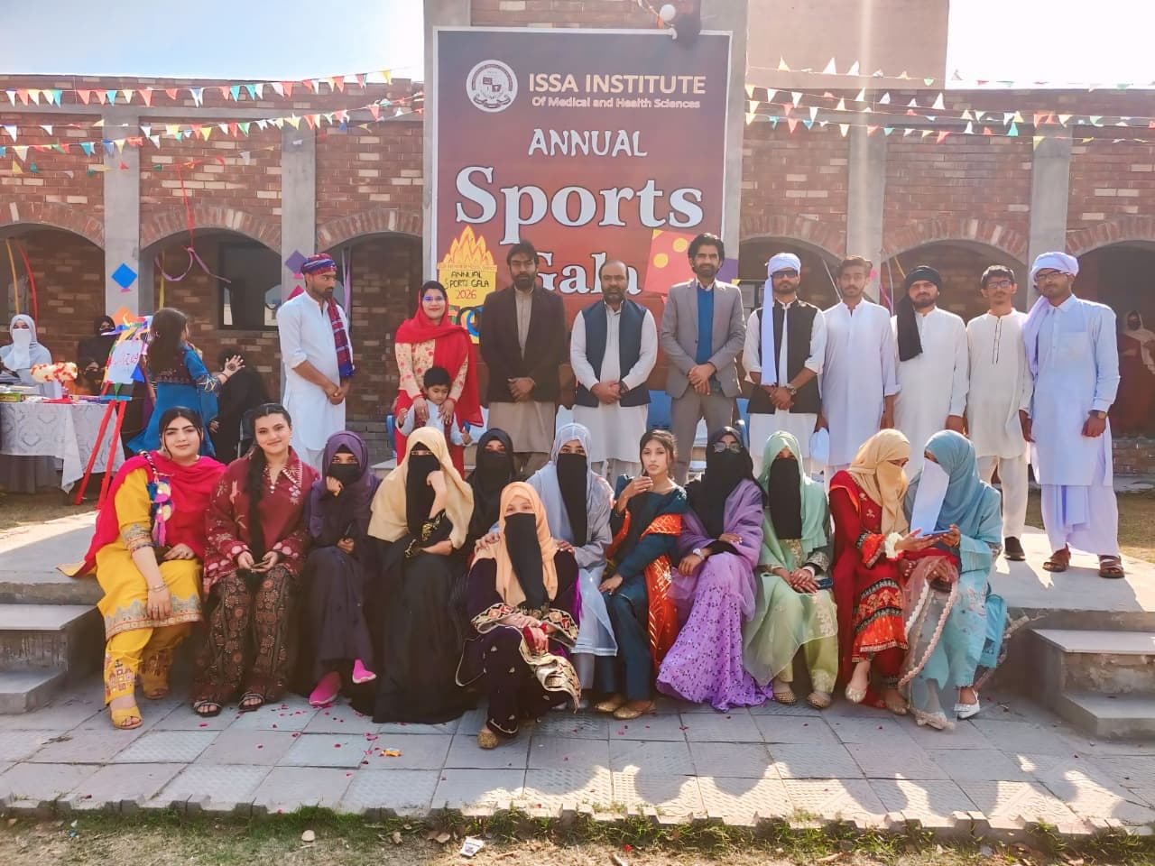 Students and faculty in traditional dress in front of the Annual Sports Gala banner