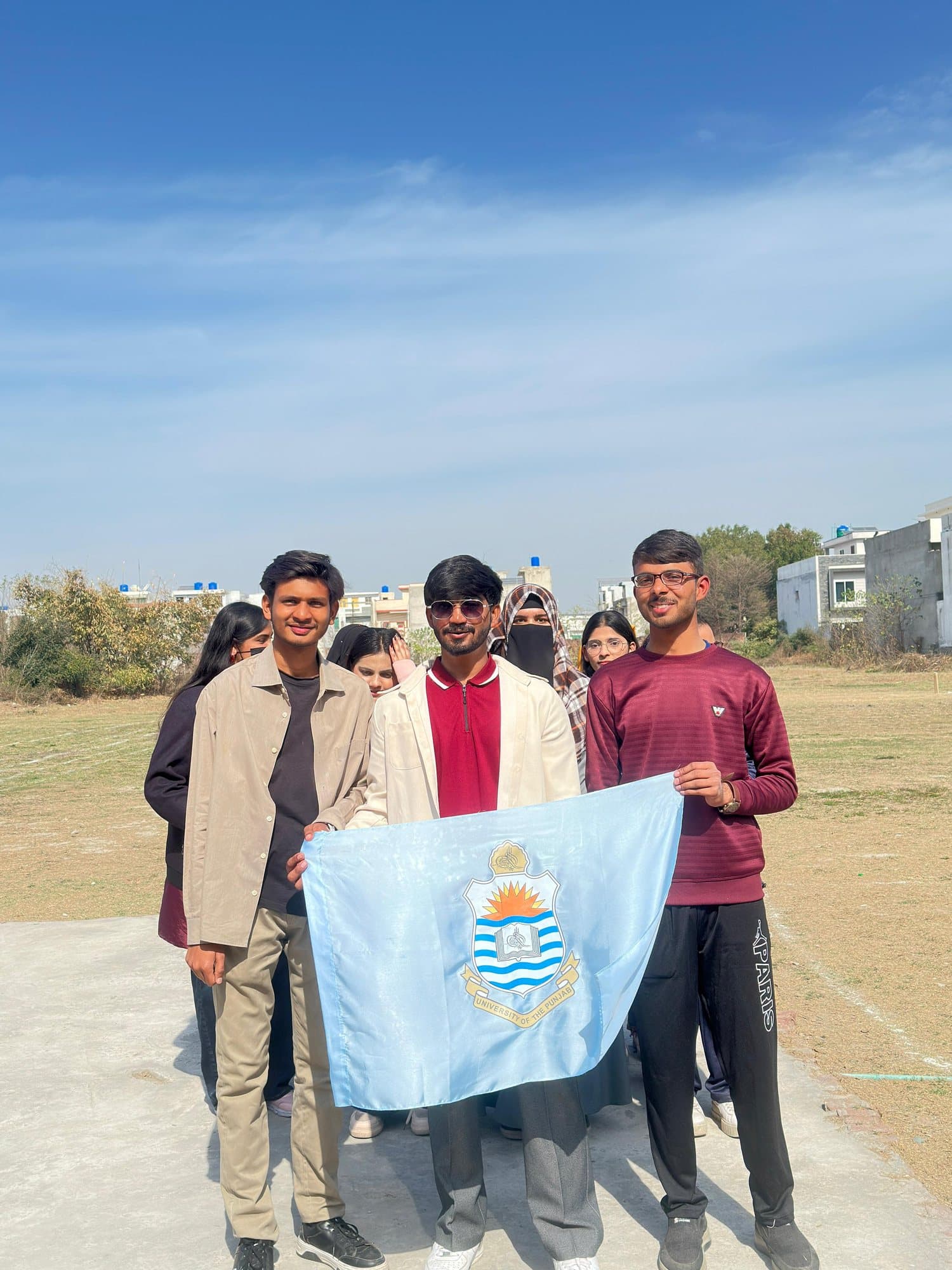 Three students holding the University of the Punjab flag on the sports ground