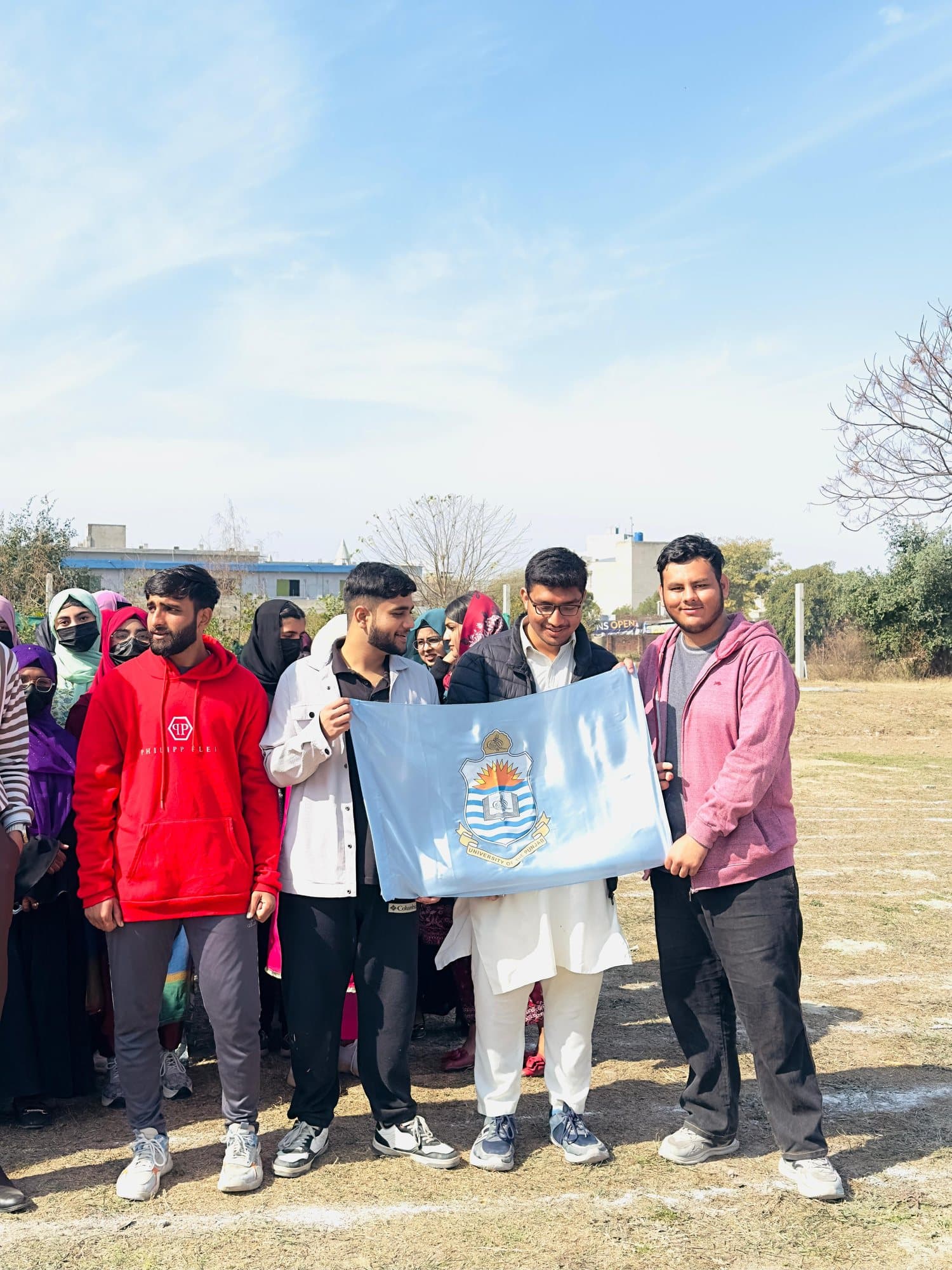 A team of students holding the University of the Punjab flag on the sports ground