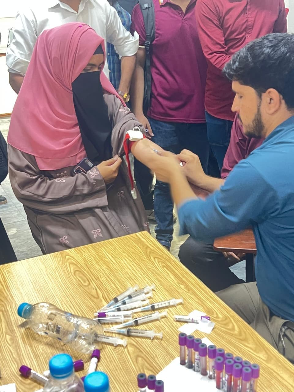 A student having a blood sample taken at the screening camp, with sample tubes on the table