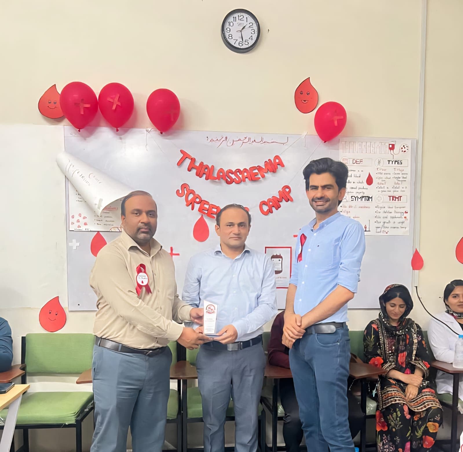 A guest receiving a souvenir shield in front of the Thalassaemia Screening Camp display at ISSA