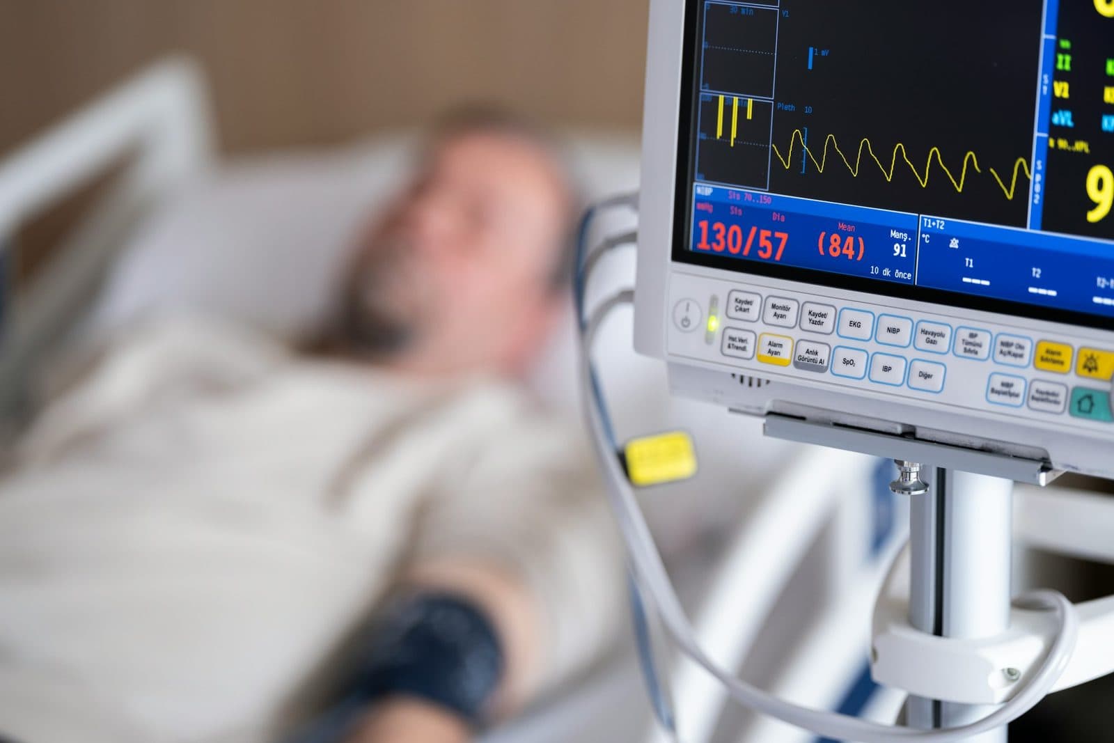 A patient in a hospital bed beside a monitor showing blood pressure and heart rate